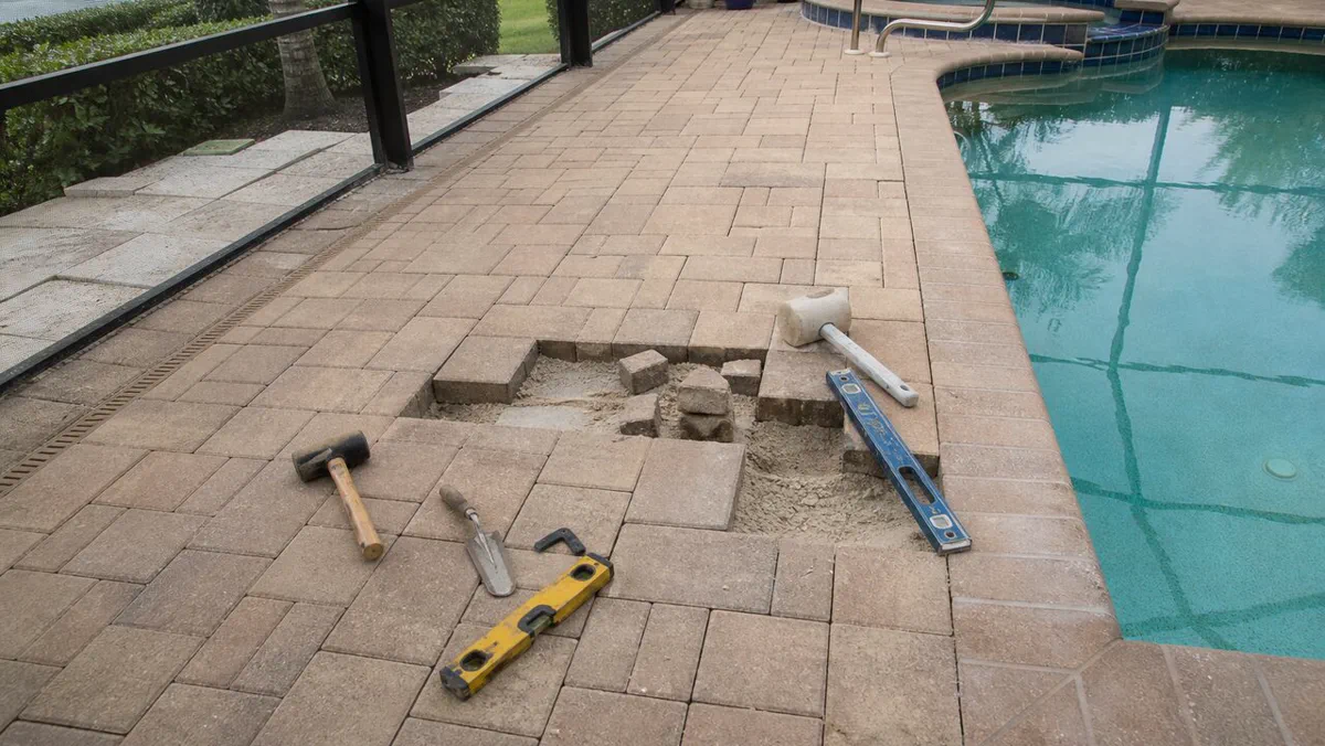 Pool deck paver repair in progress beside a screened Tampa Bay pool